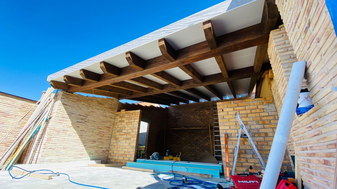 Techo con vigas de madera y paneles sandwich para un porche en una vivienda de nueva construcción